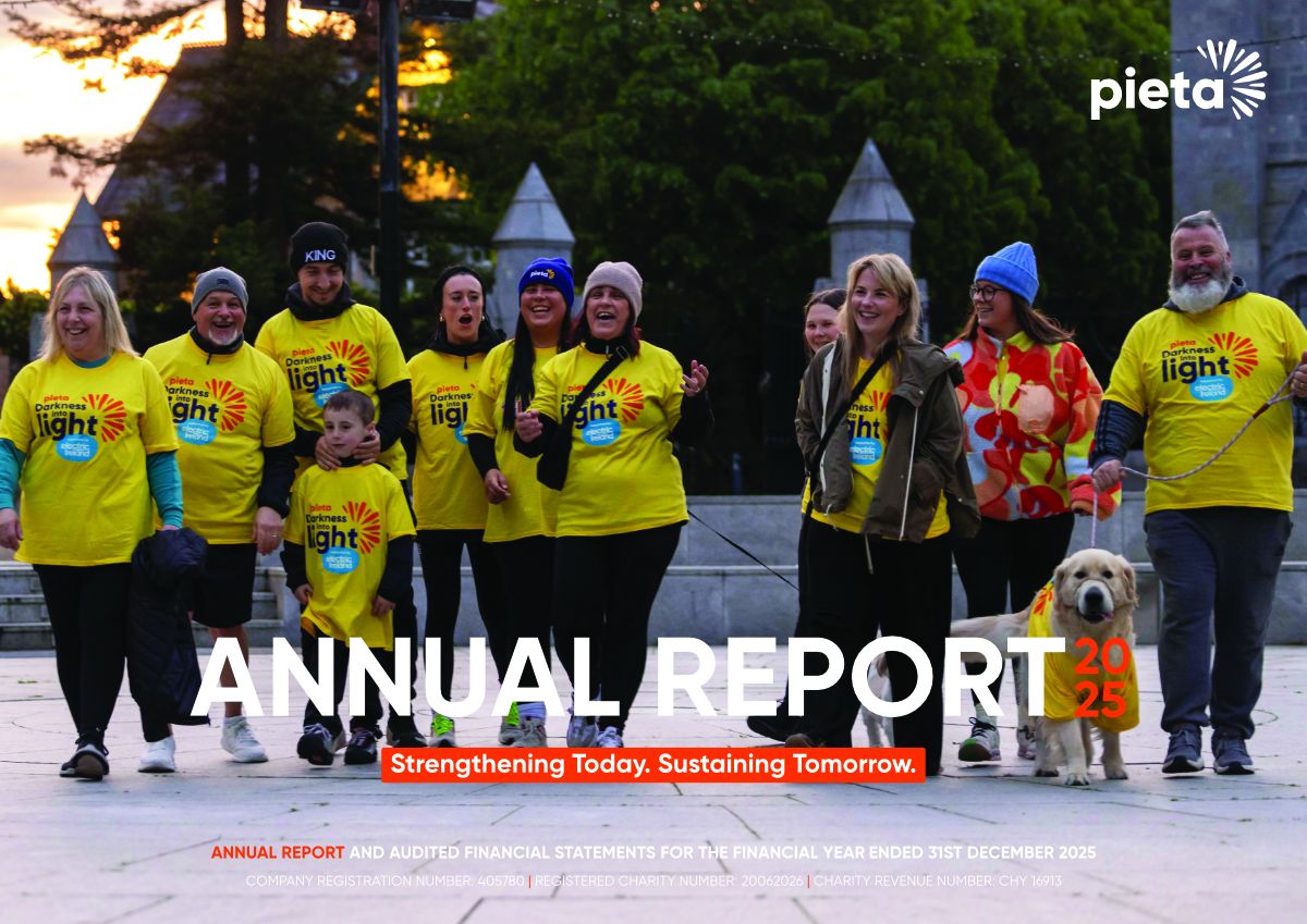A group of people, including a child and a dog, wearing yellow "Darkness into Light" shirts, walking together at dusk.
